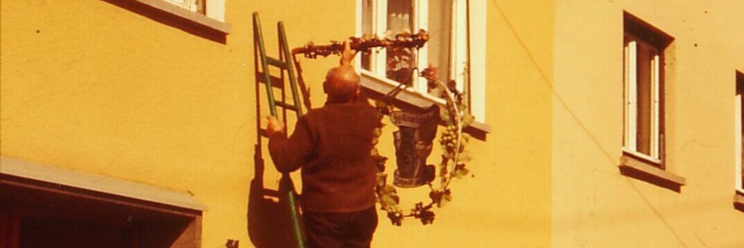 Heckenwirt und Gäste eröffnen eine Heckenwirtschaft und hängen das Schild auf.