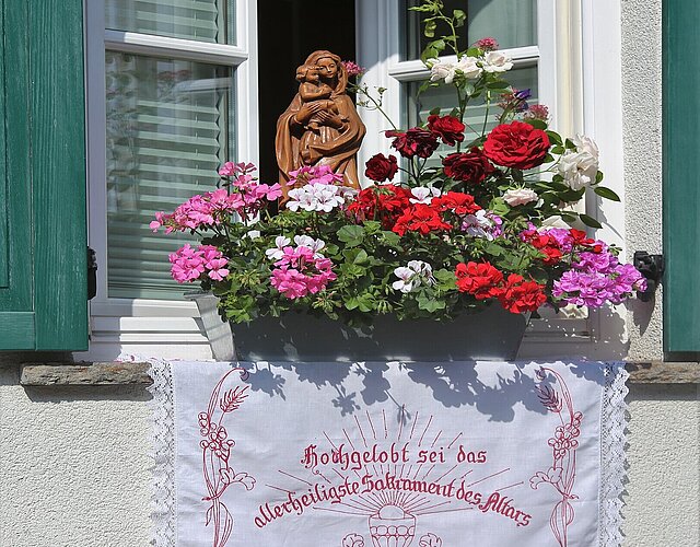 Marienfigur und Blumenschmuck an einem Fenster zur Prozession an Fronleichnam
