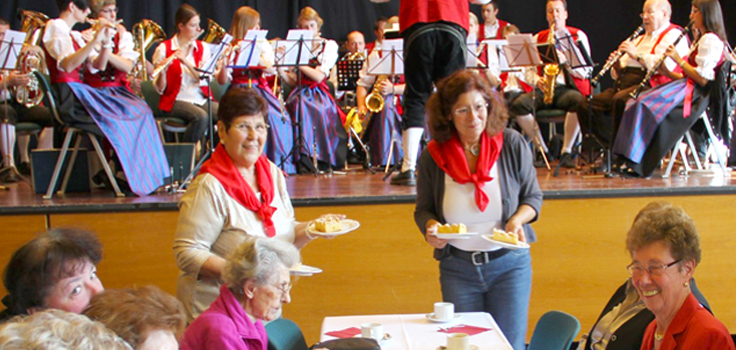 Gemeinderätinnen servieren beim Seniorennachmittag Kaffee und Kuchen. Im Hintergrund spielt der Musikverein.